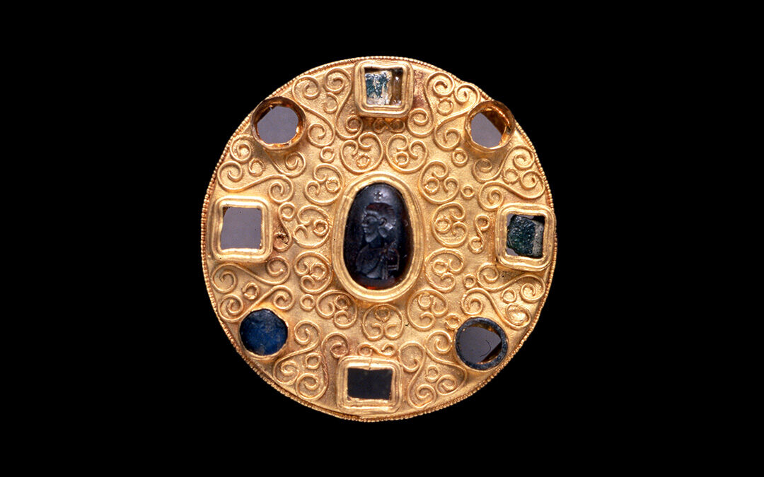 Fibula a disco in oro, con pasta vitrea e gemme incastonate